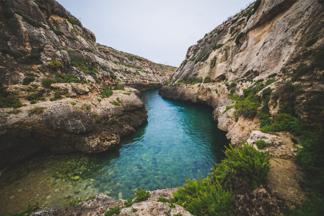 The serene, crystal-clear waters of Wied il-Għasri, hidden on Gozo’s northern coast