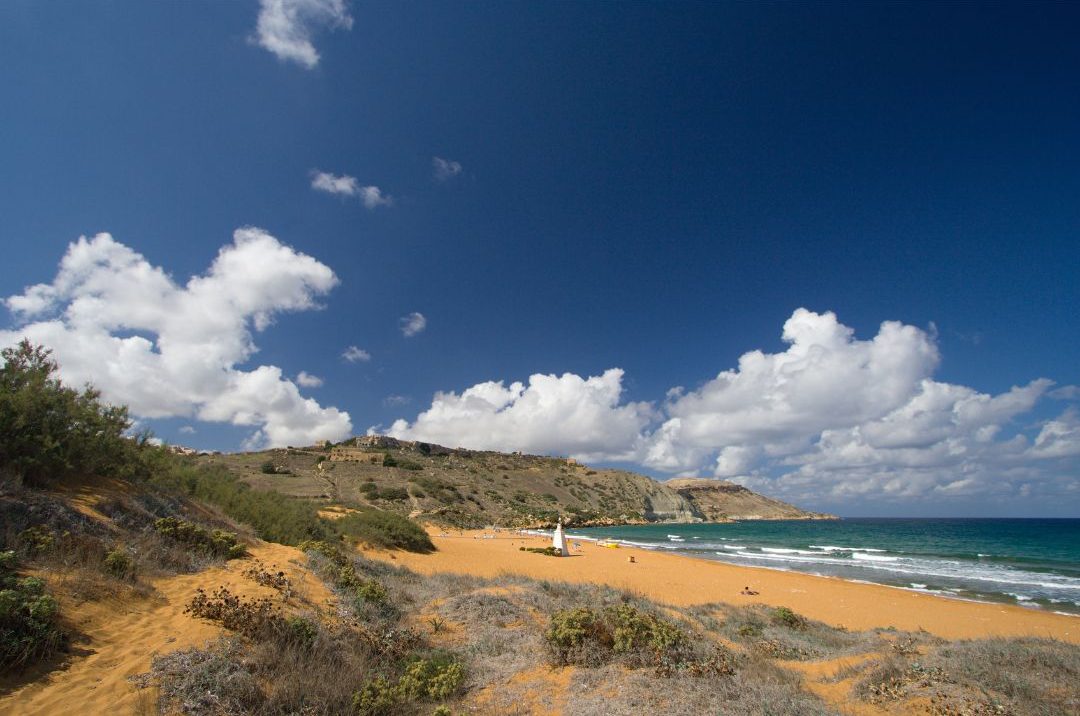 A tranquil view of Ramla Bay, showcasing its unique red sand and calm waters.