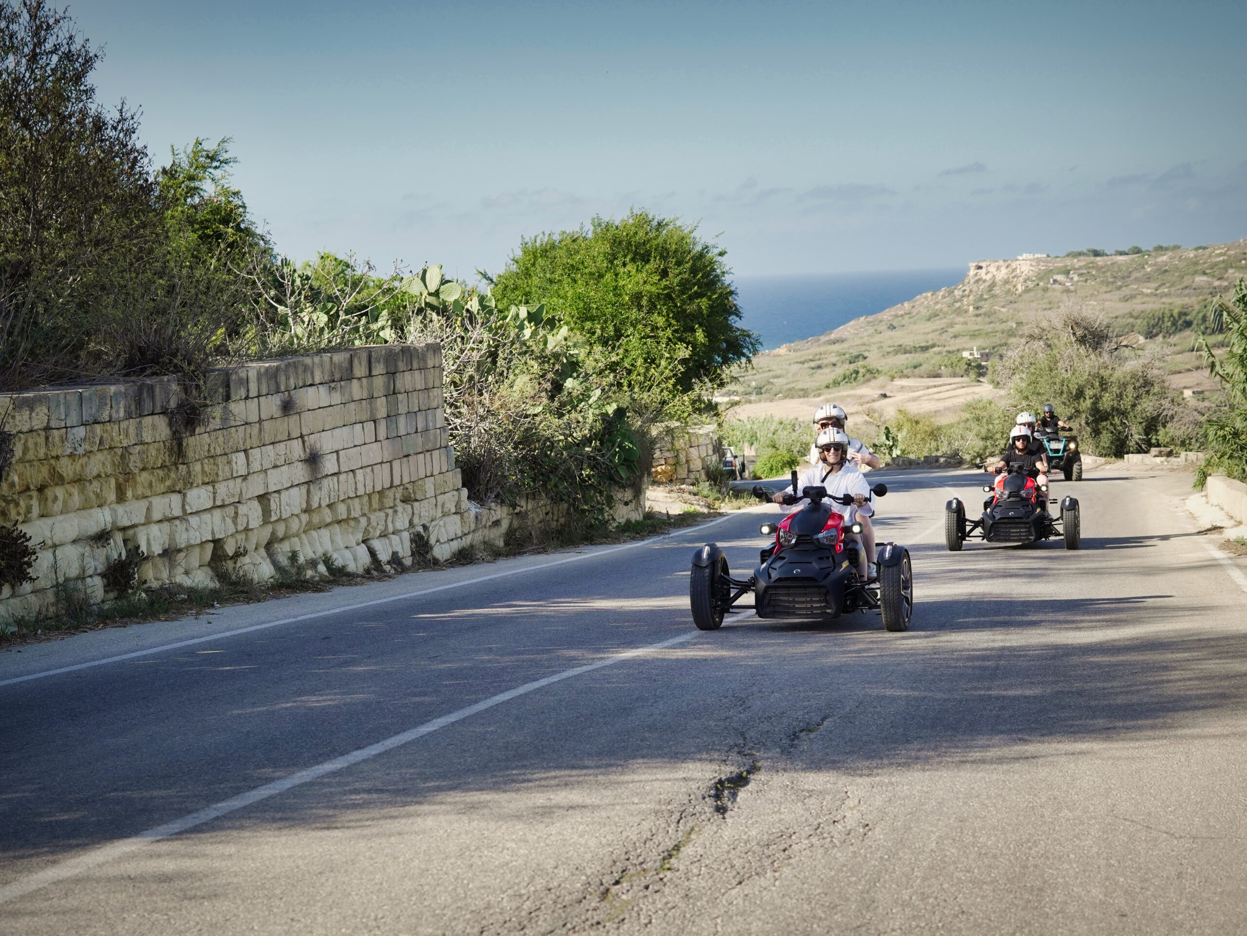 Rykers riding along a road in Gozo with stunning country and distant sea views.